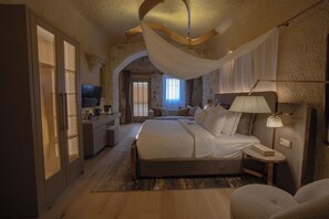 A spacious bedroom with a large bed, a television, a bedside table, and a lamp. - Alfina Cave Hotel (Urgup)