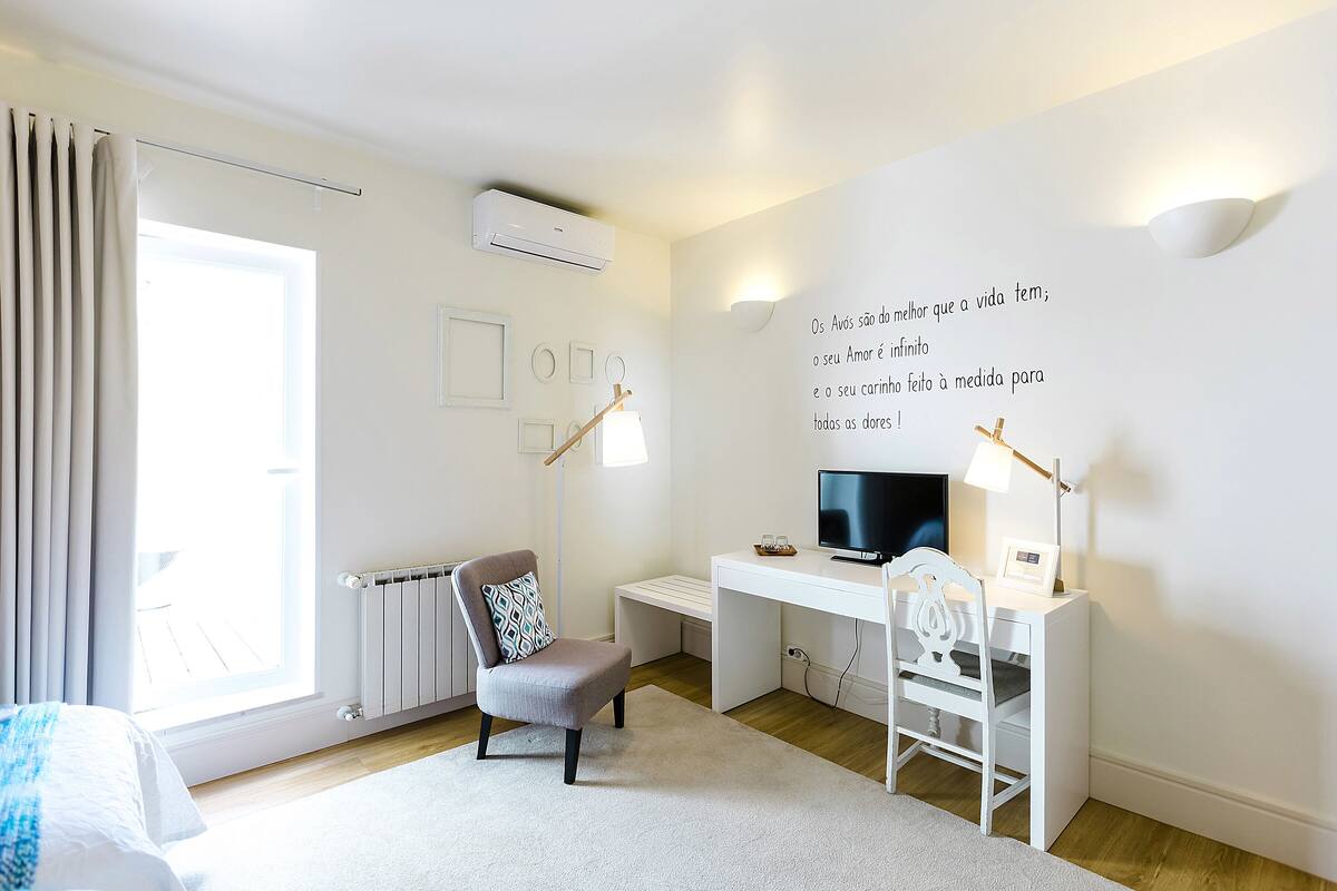 Une chambre moderne avec un lit, un bureau, une chaise, un téléviseur et un mur orné de texte.