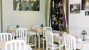 Un comedor con sillas y mesas blancas, una estantería con libros y botellas, y un cuadro en la pared.
