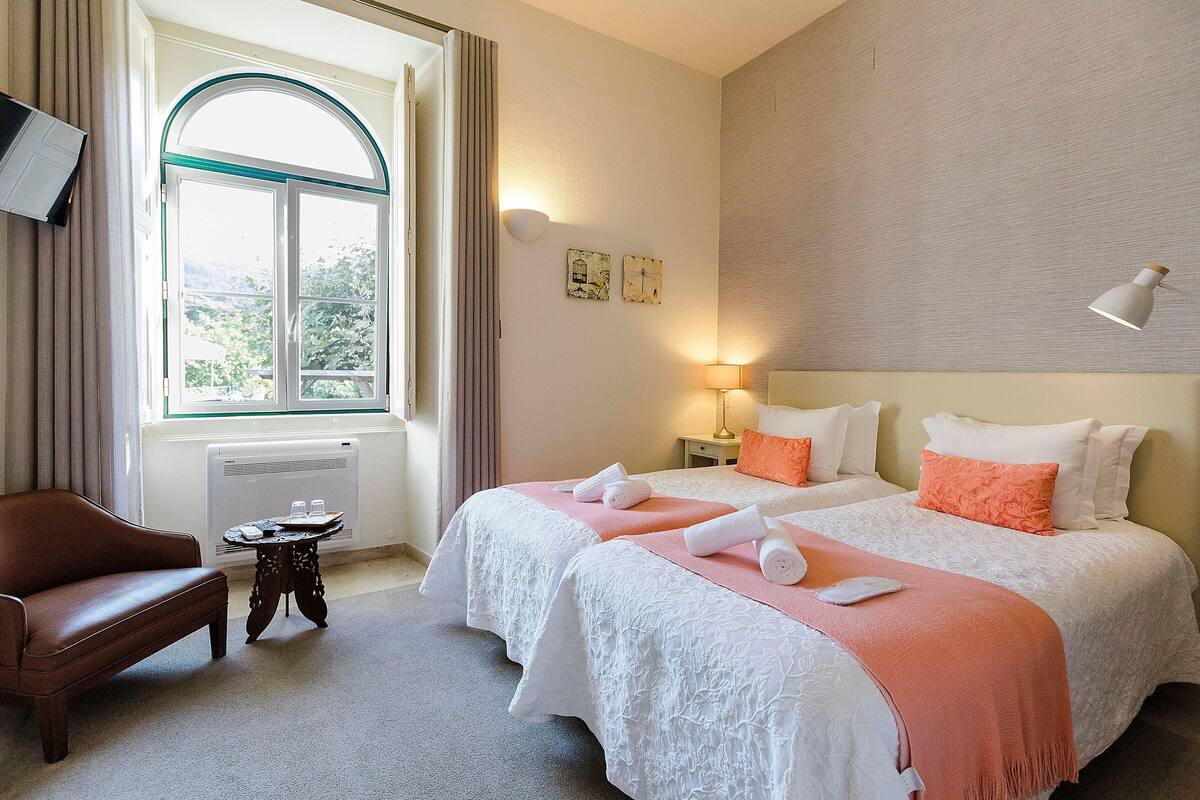 Une chambre d’hôtel avec deux lits, un canapé, une petite table et une fenêtre avec des rideaux.