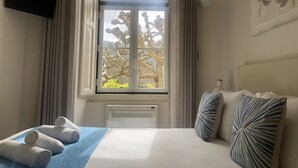 Habitación de hotel con cama, ventana con cortinas, televisor de pantalla plana y radiador.