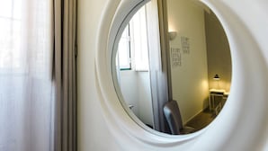 Ventana circular con vistas a un baño, que incluye un espejo, una silla y una mesita de noche con lámpara.