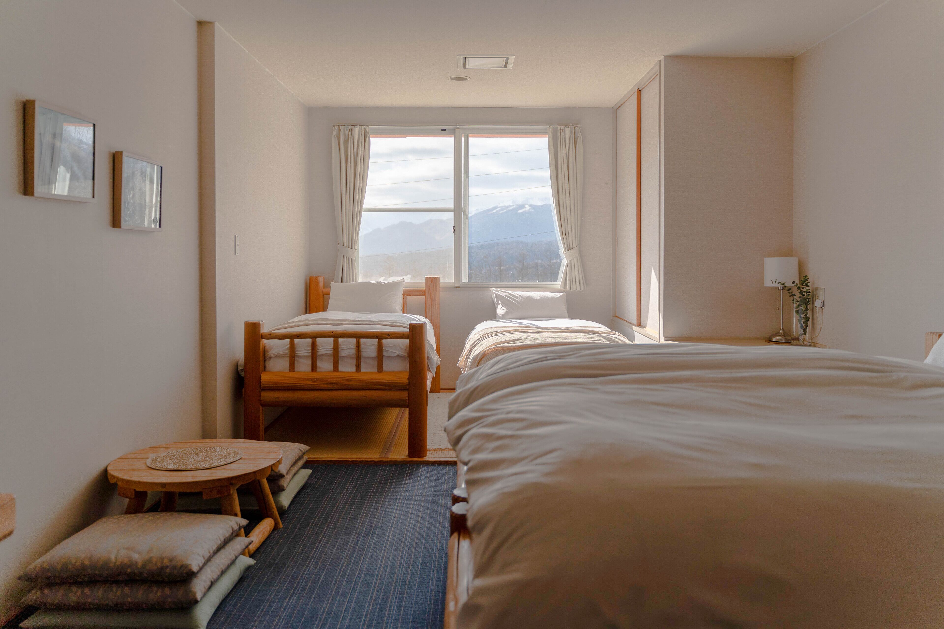 A hotel room with two beds, a small table, and a view of mountains through the window.