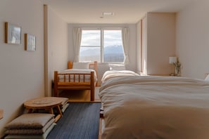 Habitación de hotel con dos camas, una mesita y vistas a las montañas a través de la ventana.