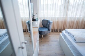 Une chambre d’hôtel avec deux lits, une chaise, un bureau avec une bouilloire et des rideaux en voile.