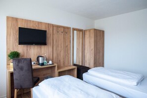 Une chambre d’hôtel avec une armoire en bois, un bureau doté d’un téléviseur à écran plat, un lit et une petite plante.