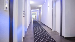 Un couloir d’hôtel moderne avec un sol carrelé, des murs blancs et des portes de part et d’autre.