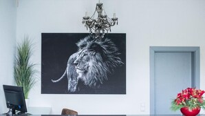 Un espace d’accueil agrémenté d’une grande œuvre d’art représentant un lion en noir et blanc, d’un lustre, d’une plante en pot, d’un vase avec une fleur rouge et d’une porte.