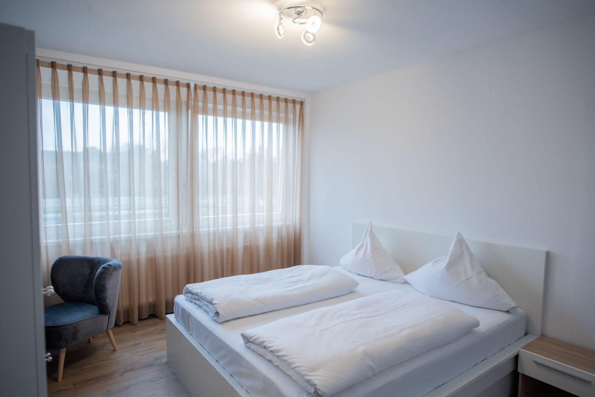 Ein modernes Hotelzimmer mit einem großen Bett, einem Sessel und einem Nachttisch.