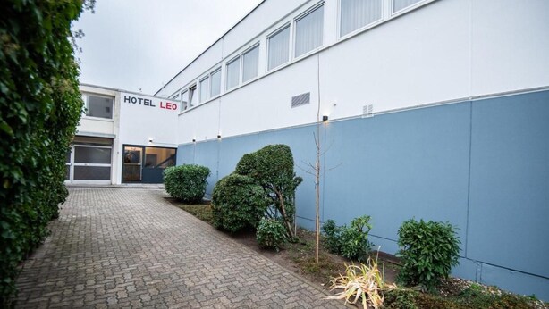 Un hôtel moderne doté d’une allée pavée, d’arbustes soigneusement taillés et d’une enseigne bien visible indiquant « HÔTEL LEO ».