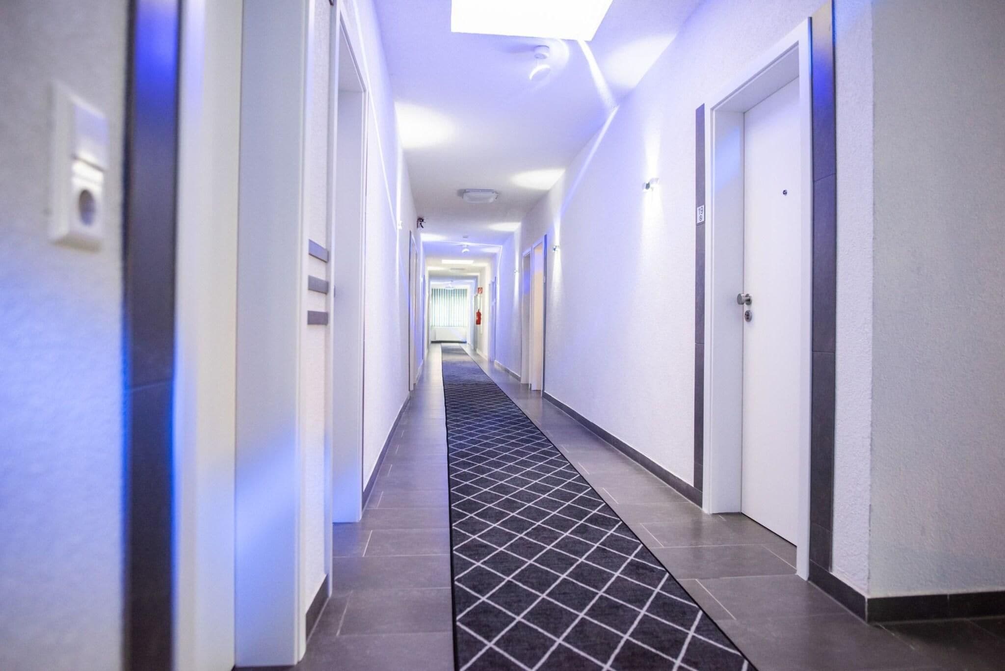 A modern hotel hallway with a tiled floor, white walls, and doors on both sides.