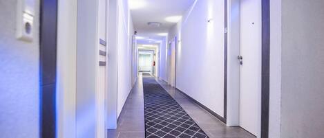 Un pasillo moderno de hotel con piso de baldosas, paredes blancas y puertas a ambos lados.