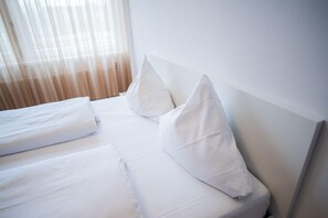 Una habitación de hotel con una cama bien hecha, ropa de cama blanca y un cabecero.