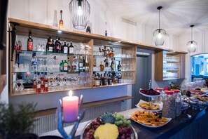 Una zona de bar con estantes llenos de botellas de licor y vasos, una vela y una bandeja de frutas.
