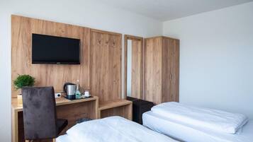 Ein Hotelzimmer mit Holzschrank, Schreibtisch mit Flachbildfernseher, Bett und einer kleinen Pflanze.
