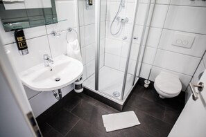 Un baño moderno con cabina de ducha de vidrio, un lavamanos blanco y un inodoro.
