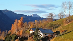 Ett hus på landsbygden med ett sluttande tak, omgivet av träd i höstfärger och med ett berg i bakgrunden.