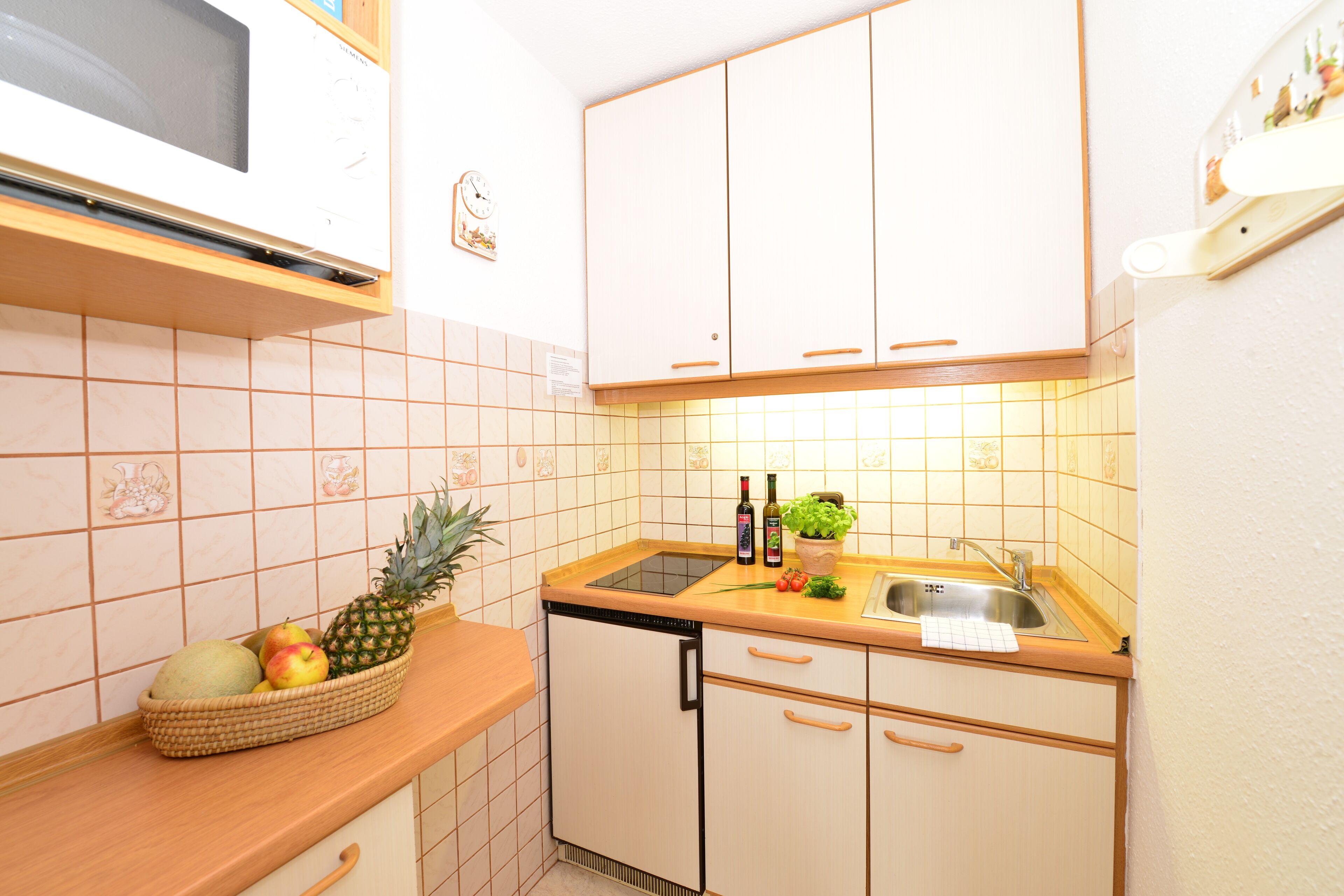 A kitchen with white cabinets, a microwave, a sink, and a fruit basket on the counter.
