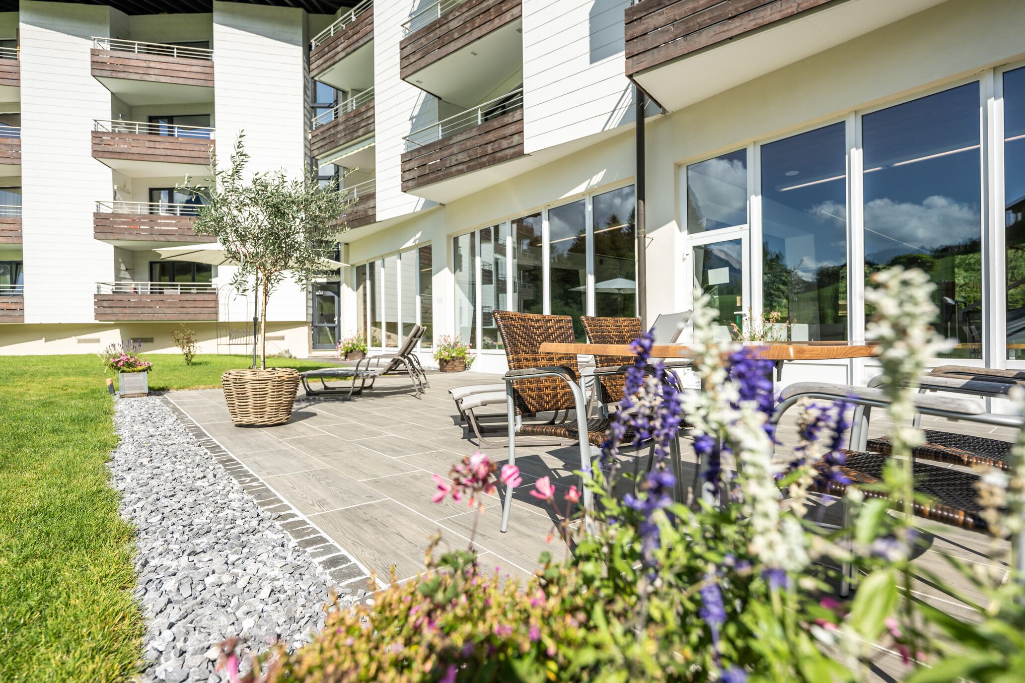 A modern apartment building with a patio area featuring outdoor furniture and a small tree.