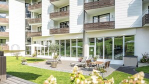 A modern apartment building with balconies, a patio area with outdoor furniture, and a well-maintained lawn. - Familienhotel Kleinwalsertal (Mittelberg)