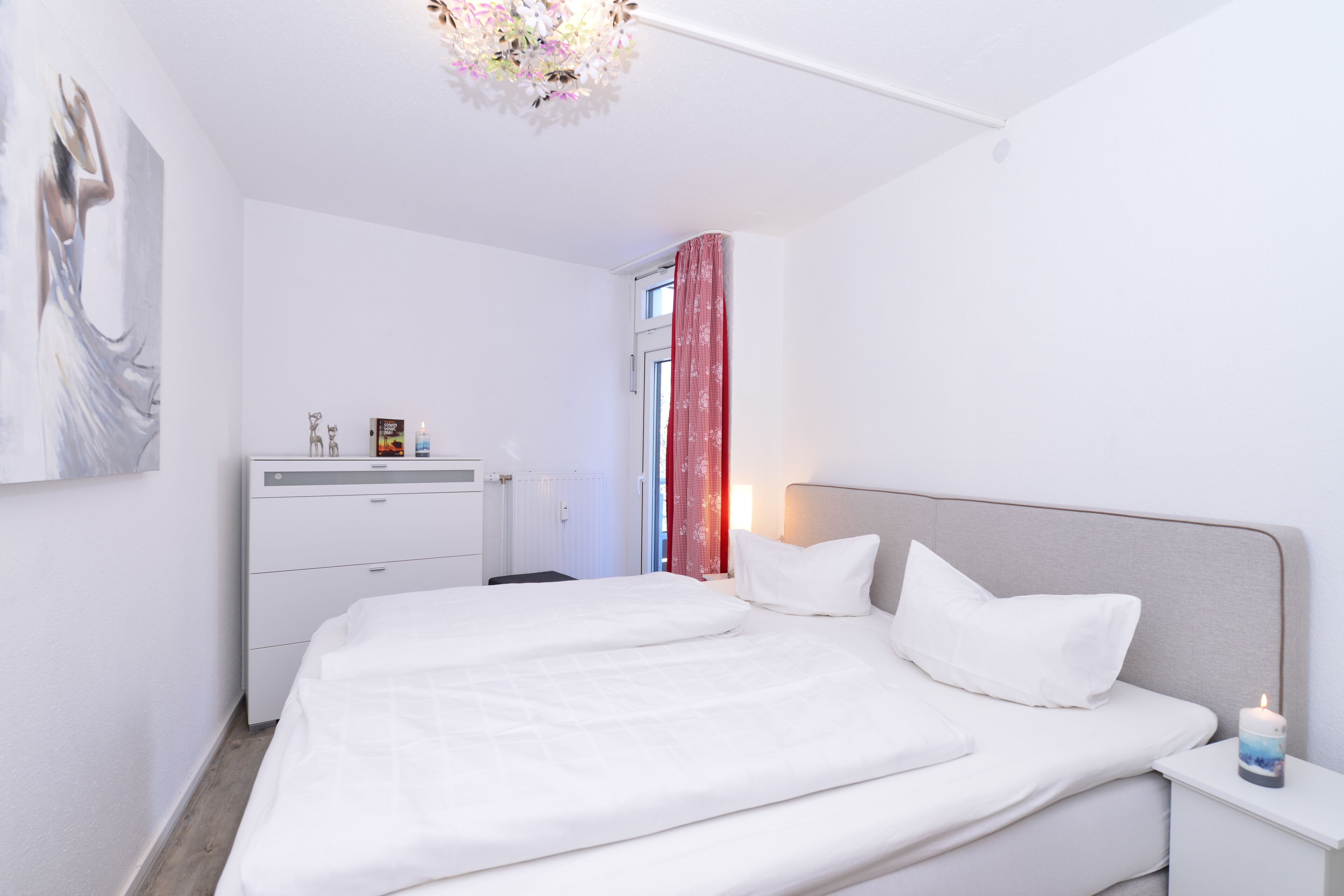 A modern bedroom with a large bed, bedside tables, a dresser, and a painting on the wall.