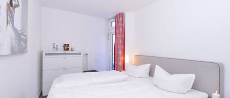 A modern bedroom with a large bed, bedside tables, a dresser, and a painting on the wall.