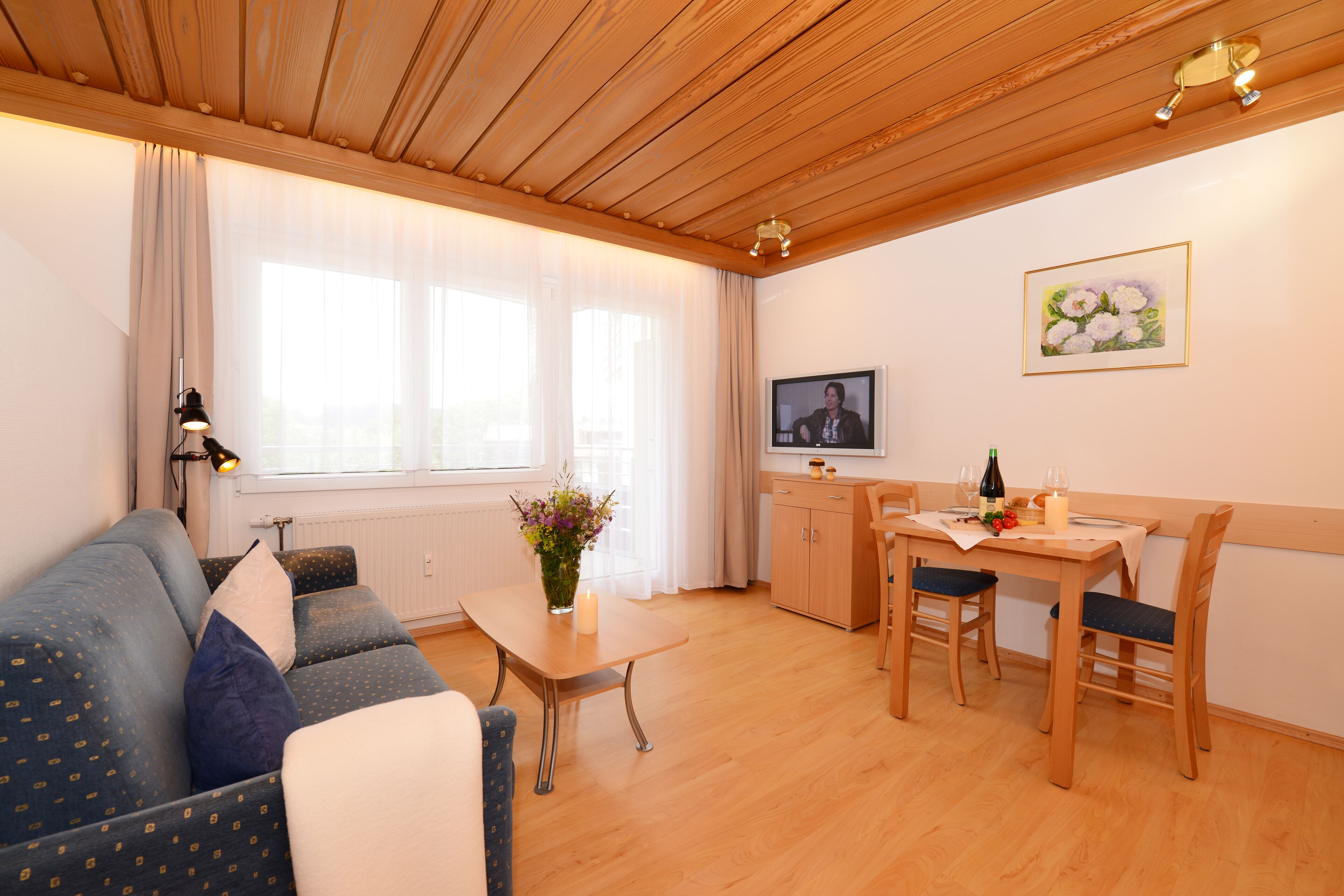 A cozy living room with a sofa, a dining table with chairs, a TV, and a wooden ceiling.