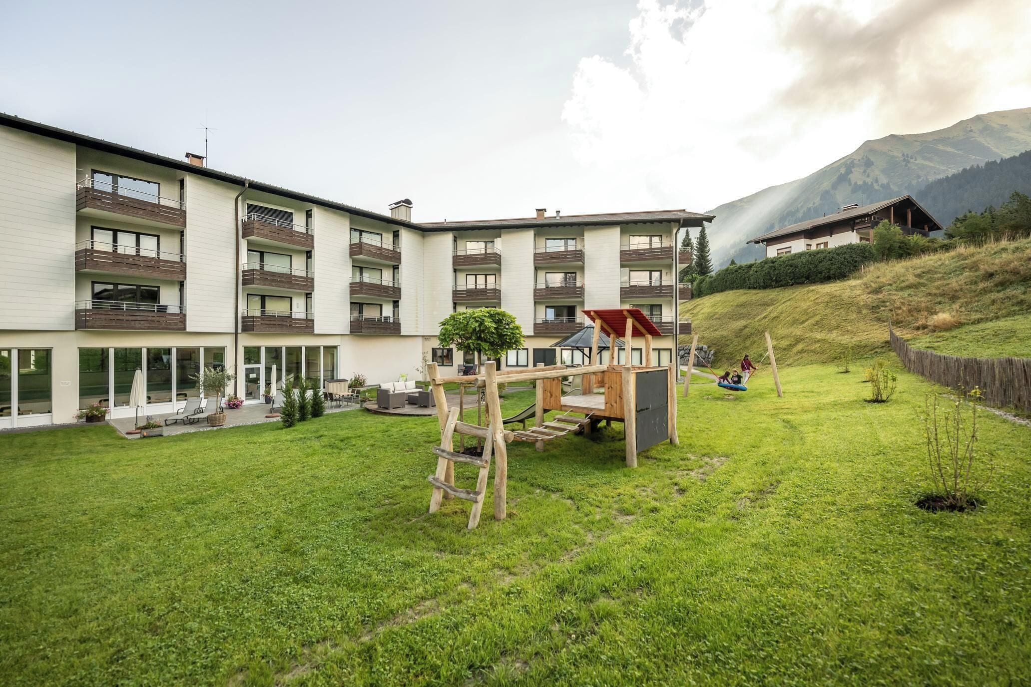A multi-story building with balconies, a grassy courtyard, and a mountain backdrop.