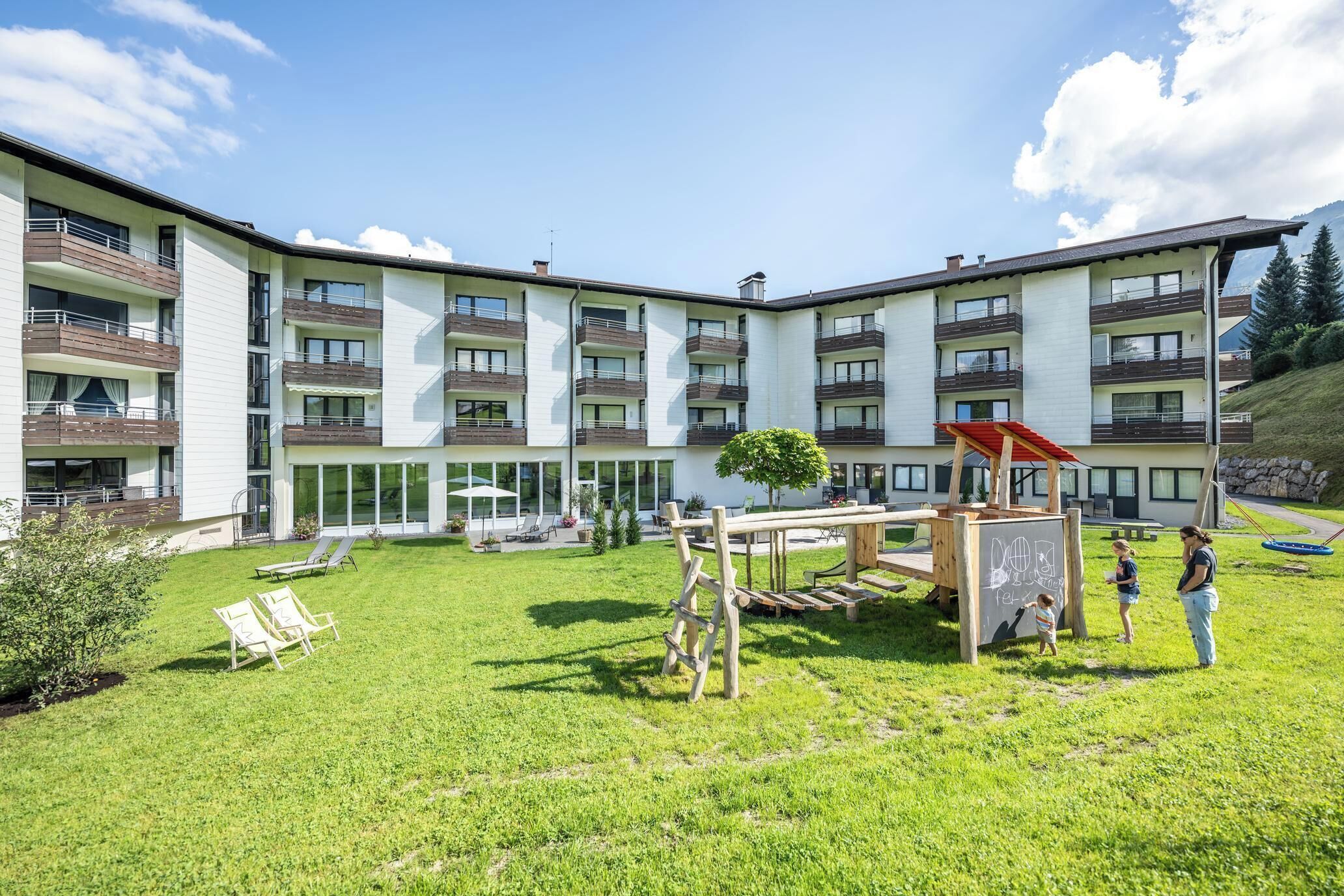 Un immeuble d’appartements moderne doté de nombreux balcons, d’une cour verdoyante avec des espaces de détente en plein air et d’une aire de jeux pour enfants.
