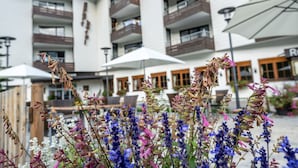 A hotel with multiple balconies, outdoor seating, and a variety of flowers in the foreground. - Familienhotel Kleinwalsertal (Mittelberg)