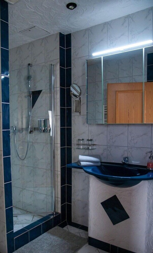 A bathroom with a glass-enclosed shower, a sink with a blue countertop, and a mirror above the sink. - Am Edersee (Edertal)