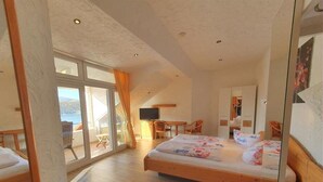 A bedroom with a wooden bed, a desk, and a chair, a television, and a large window with curtains. - Am Edersee (Edertal)