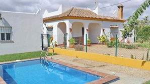 A swimming pool with a ladder, surrounded by a fenced area with potted plants and a building with a tiled roof. - Chalet Pilahito with private pool (CONIL DE LA FRONTERA)