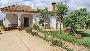 A white building with a tiled roof, a bench, and potted plants in the garden area. - Chalet Pilahito with private pool (CONIL DE LA FRONTERA)