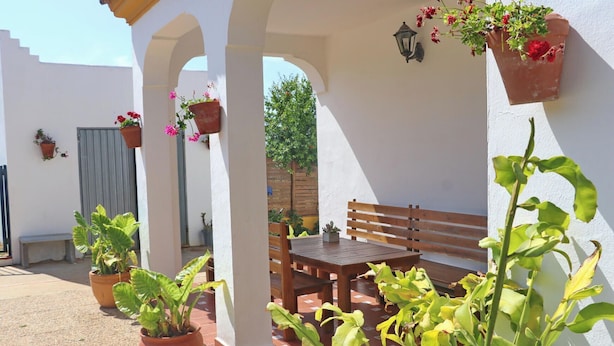 An outdoor patio with a wooden bench and table, surrounded by potted plants and a white wall. - Chalet Pilahito with private pool (CONIL DE LA FRONTERA)