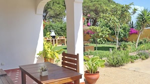A patio with a wooden table and chairs, surrounded by a garden with various plants and a barbecue area in the background. - Chalet Pilahito with private pool (CONIL DE LA FRONTERA)