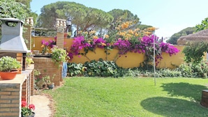 A garden with a yellow wall, potted plants, and a barbecue area. - Chalet Pilahito with private pool (CONIL DE LA FRONTERA)