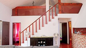 A spacious living area with a high ceiling, a wooden staircase, and a kitchen area with a tiled backsplash.