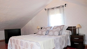 A bedroom with a bed, two bedside tables, a window with curtains, and a sloped ceiling.