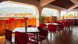 A restaurant with red chairs and tables, large windows, and a view of mountains. - Hotel Alcaravan (Medellin)
