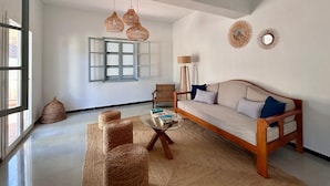 A living room with a sofa, two chairs, a coffee table, wicker ottomans, a floor lamp, and a window with shutters. - Ca sa Madona (Calvià)