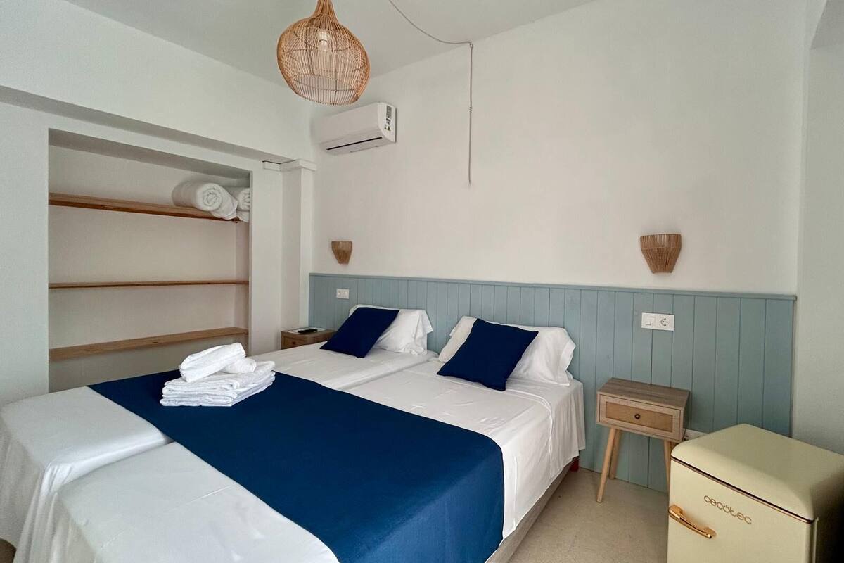 A bedroom with a bed, a bedside table, a wardrobe, and a small refrigerator.