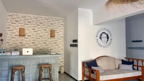 A room with a patterned wallpaper, a wooden sofa, a wicker chair, a laptop on a counter, and a wall-mounted circular emblem. - Ca sa Madona (Calvià)