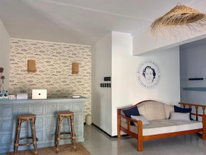 A room with a patterned wallpaper, a wooden sofa, a wicker chair, a laptop on a counter, and a wall-mounted circular emblem. - Ca sa Madona (Calvià)