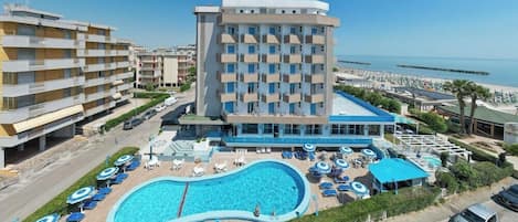 A hotel with a swimming pool, multiple balconies, and a view of the sea.