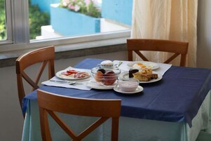 A table set with plates of food, including a bowl of fruit, a glass of milk, and a plate with a slice of cake, in a room with a view of a blue exterior.