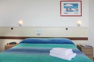 Una habitación de hotel con cama, mesita de noche, luz en la pared y un cuadro enmarcado.