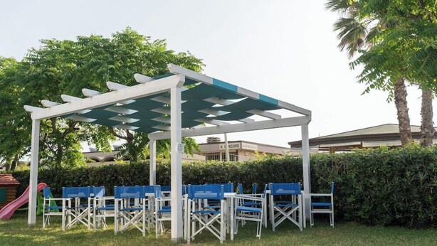 An outdoor seating area with a pergola, blue chairs, and a playground. - Concord (Ravenna)