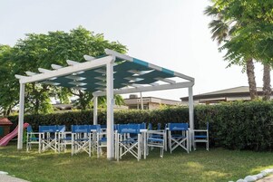Un área de estar al aire libre con una pérgola, sillas azules y un parque infantil.