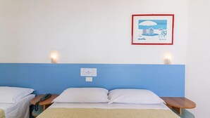 Habitación de hotel con una cama individual, mesitas de noche, teléfono en la pared y un cuadro enmarco.
